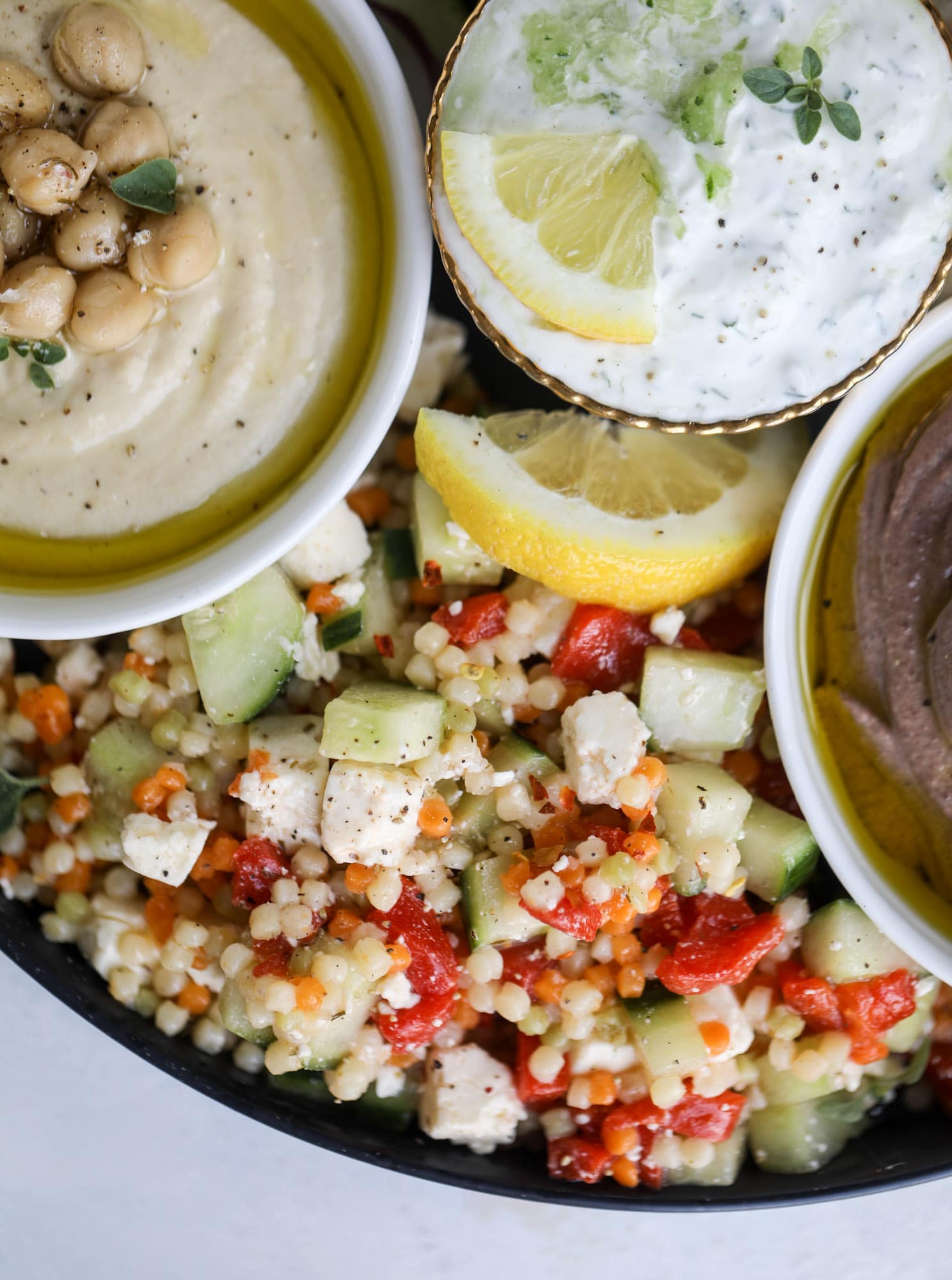 Here you can find out how to make the perfect hummus platter! This trio includes caramelized onion hummus, smoky black bean hummus and roasted red pepper white bean hummus, along with a couscous salad and quick tzatziki! I howsweeteats.com #hummus #platter #appetizer #snack #chickpeas #healthy #blackbeans #yogurt #tzatziki