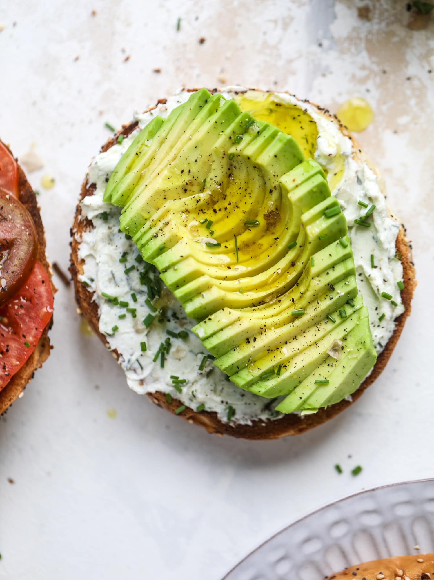 These avocado tomato sandwiches are the perfect lunch! Complete with veggie cream cheese, smoked sea salt, fresh chives and microgreens, the sliced avocado and heirloom tomatoes are sandwiched on an everything bagel for a flavor explosion. I howsweeteats.com #avocado #tomato #sandwich #healthy #lunch