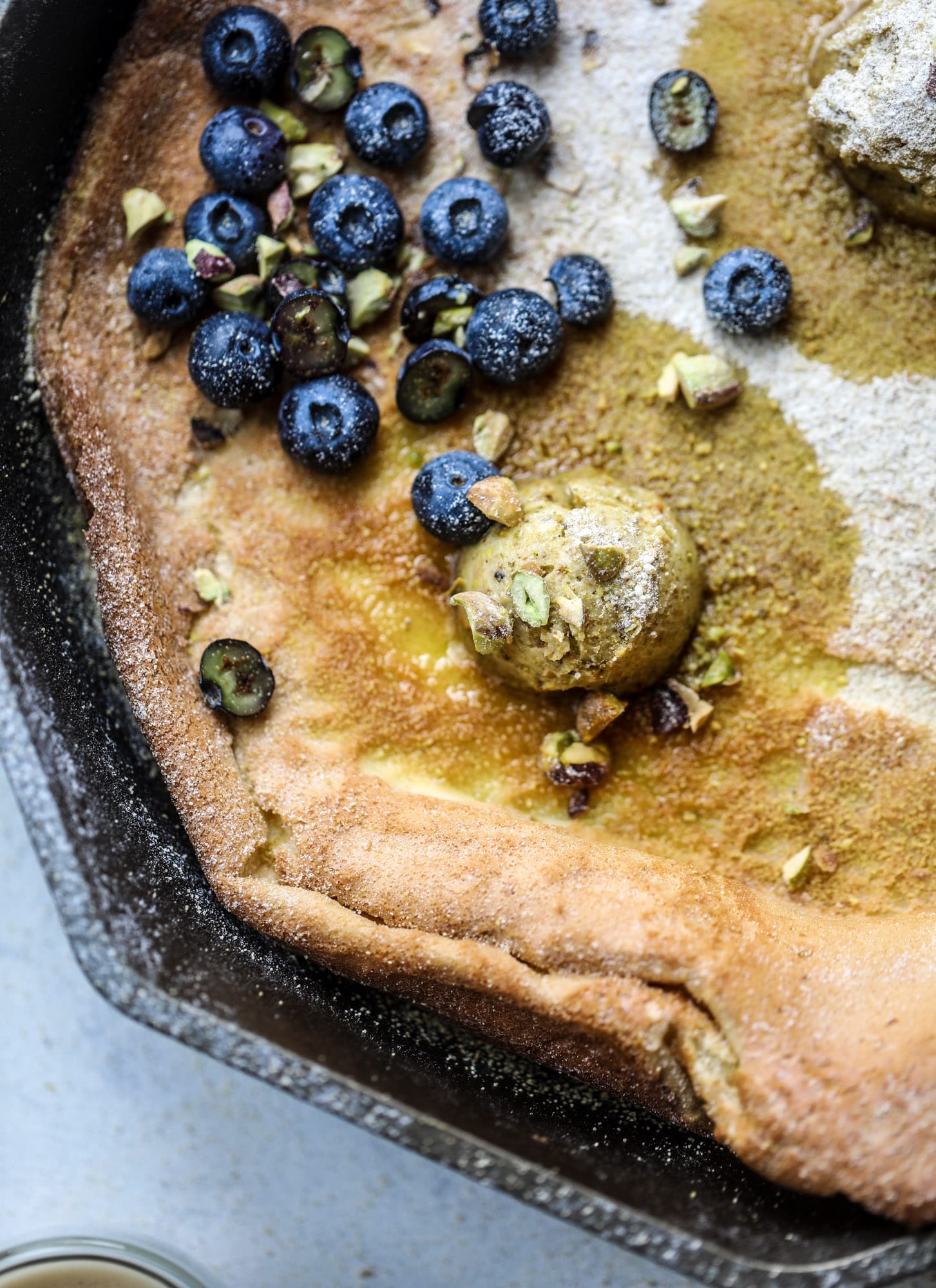 This incredible dutch baby recipe is fluffy and light and perfect for breakfast! It's sprinkled with pistachio sugar and served with pistachio butter and fresh blueberries. It's super easy, simple and always a hit! I howsweeteats.com #dutch #baby #pistachio #blueberry #breakfast