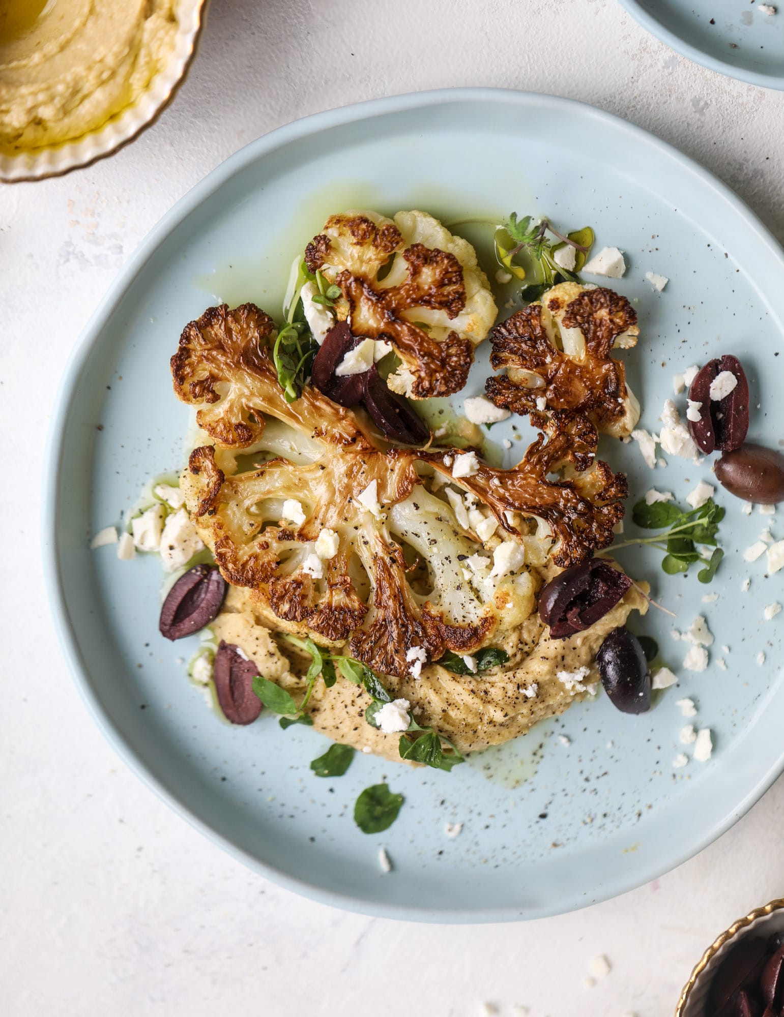 This roasted cauliflower with hummus, olives and feta is super flavorful and a wonderful meal, side dish or snack. Flavorful roasted cauliflower, creamy hummus, briney olives and tangy feta come together to make a major taste explosion. I howsweeteats.com #roasted #cauliflower #hummus #olives #feta
