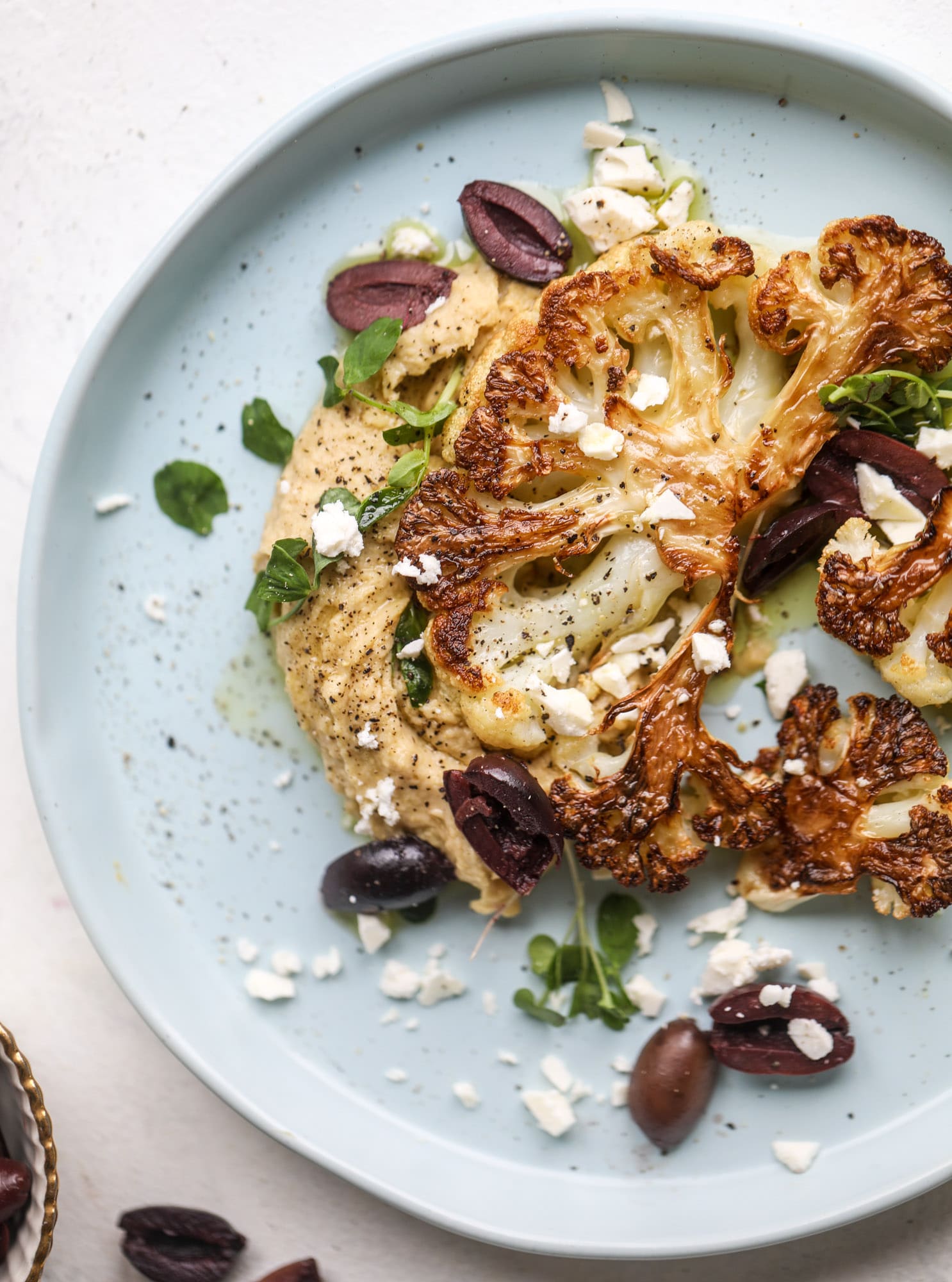 This roasted cauliflower with hummus, olives and feta is super flavorful and a wonderful meal, side dish or snack. Flavorful roasted cauliflower, creamy hummus, briney olives and tangy feta come together to make a major taste explosion. I howsweeteats.com #roasted #cauliflower #hummus #olives #feta