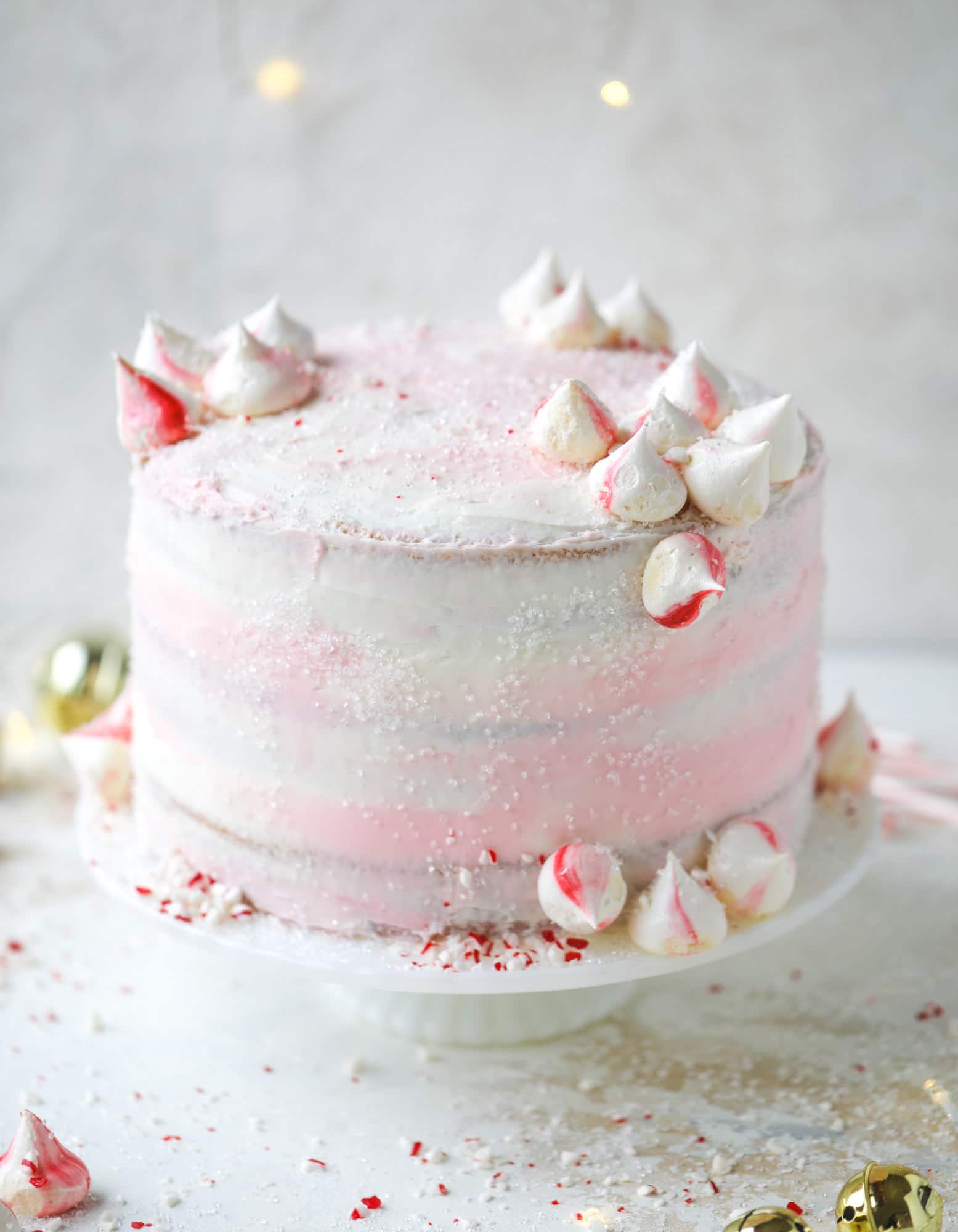 This pink peppermint cake is festive and delicious for the holidays! Layers of vanilla cake frosting with peppermint cream cheese frosting, covered in sparkly sugar and peppermint meringues. Couldn't be cuter! I #pinkpeppermint #cake
