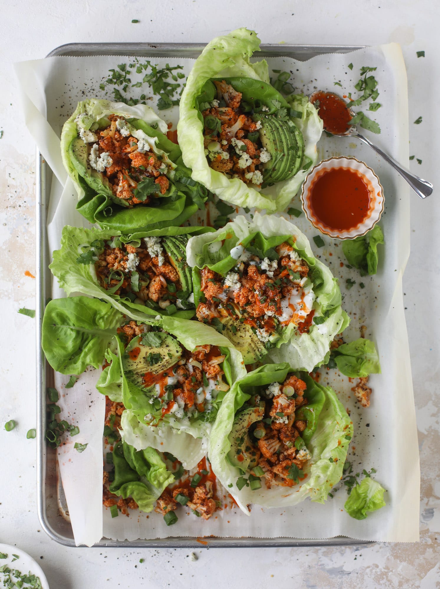 These buffalo cauliflower lettuce wraps are perfect for game day or even a quick weeknight dinner. Roasted cauliflower with buffalo wing sauce, sliced avocado, crumbled blue cheese, scallions, cilantro and chives makes for a flavor explosion! I howsweeteats.com #buffalo #cauliflower