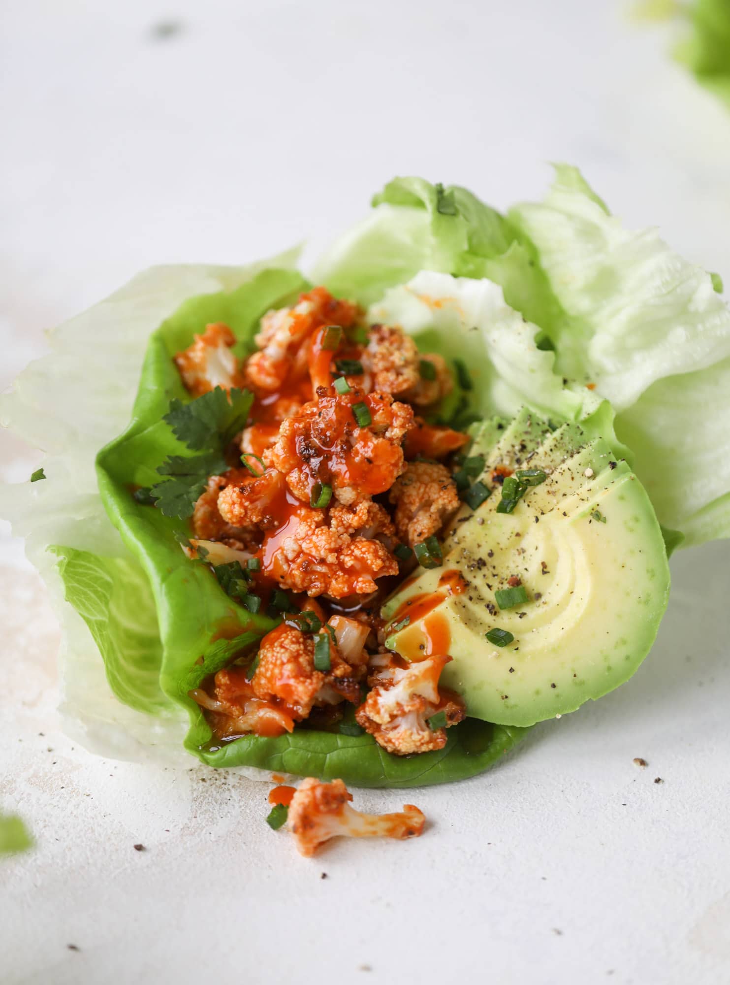 These buffalo cauliflower lettuce wraps are perfect for game day or even a quick weeknight dinner. Roasted cauliflower with buffalo wing sauce, sliced avocado, crumbled blue cheese, scallions, cilantro and chives makes for a flavor explosion! I howsweeteats.com #buffalo #cauliflower