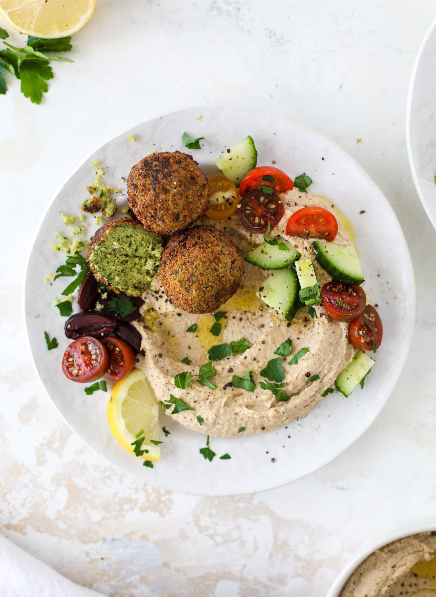 Green goddess falafel is hearty and flavorful, served over the creamiest cauliflower hummus, with tomatoes, olive, cucumbers and feta. Yum! I howsweeteats.com #falafel #cauliflowerhummus