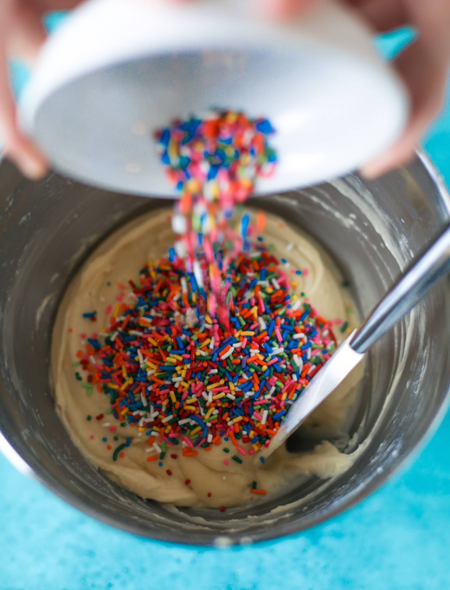 pouring rainbow sprinkles into cake batter