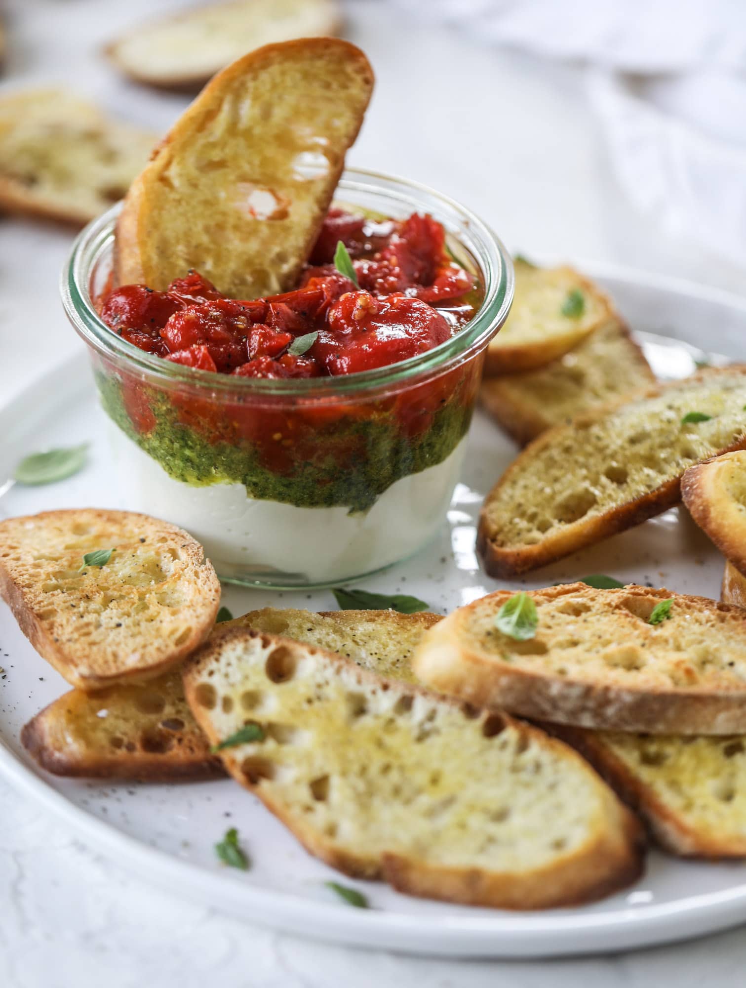 This ricotta jam jar is the perfect appetizer and snack to serve at a party! Based on the ricotta jam jar served at Nordstrom Cafe, it starts with creamy ricotta, is topped with flavorful basil pesto and a quick tomato jam. Serve with crunchy bread and dip dip dip! I howsweeteats.com #ricotta #jam #jar #nordstrom #tomato #pesto #appetizer #dip