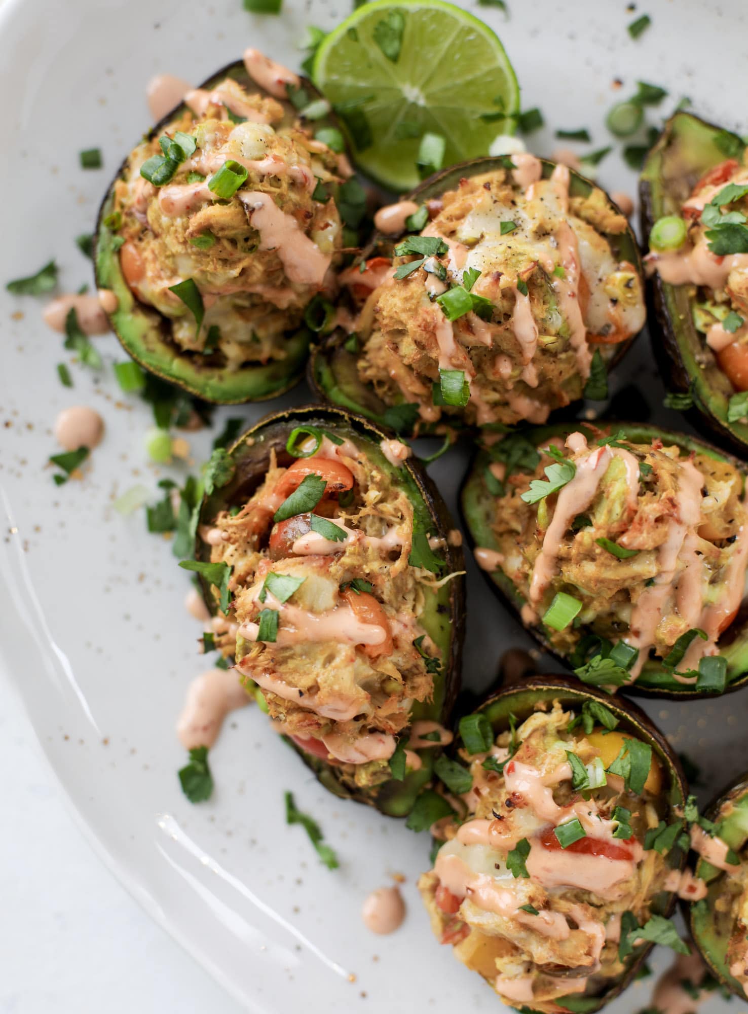 These baked avocados are stuffed with a cheesy chicken mixture and drizzled with sriracha yogurt sauce! Super delicious and an easy weeknight meal. I howsweeteats.com #baked #avocados