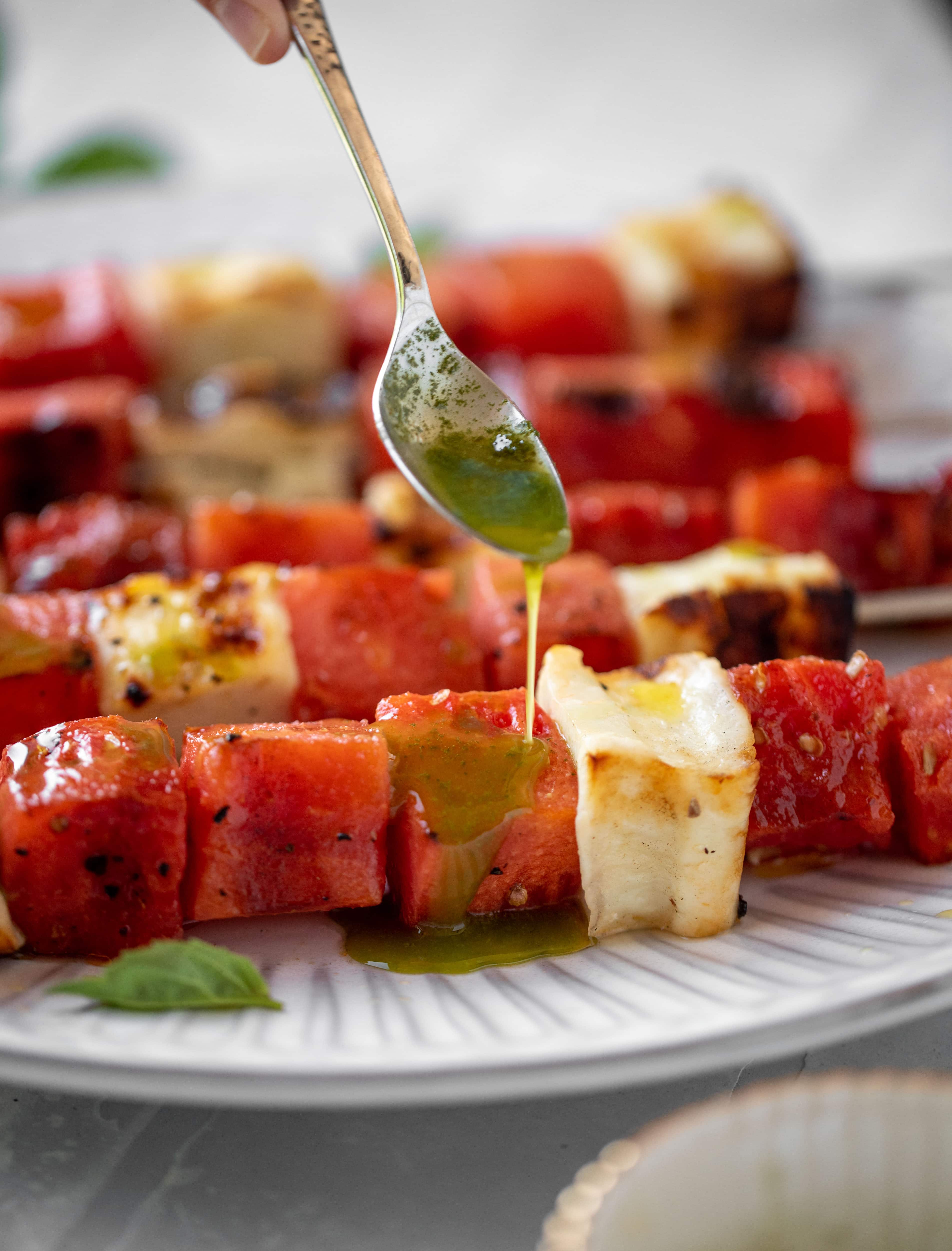 drizzling mint basil oil on grilled watermelon halloumi skewers