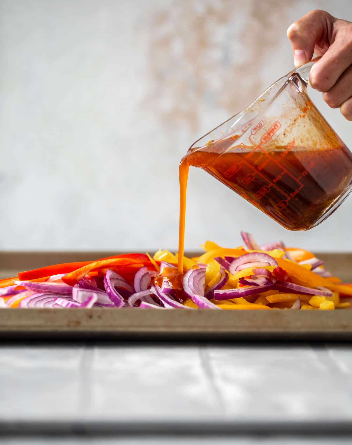 pouring fajita marinade on peppers and onions