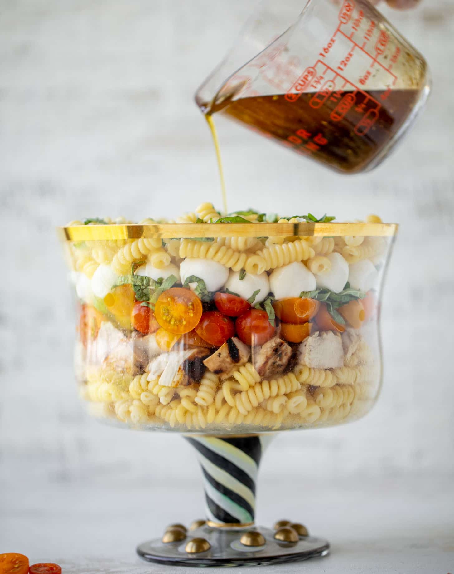 pouring dressing on grilled chicken caprese pasta salad
